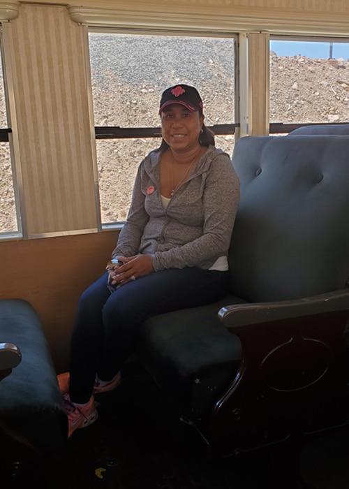 Alene with full set of hair sitting in a train with a breast cancer awareness pin on her sweater